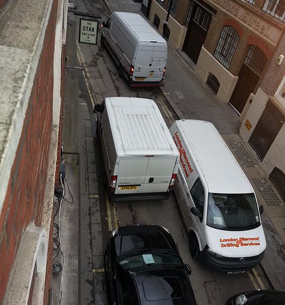 Large vehicles blocking a narrow Soho street